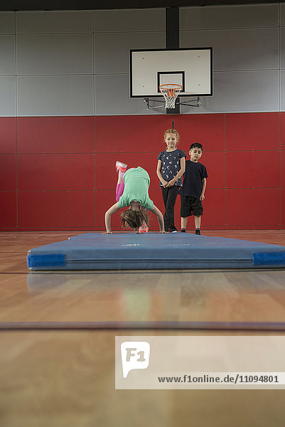 Mädchen macht Purzelbaum auf Übungsmatte in Sporthalle mit ihren Freunden  München  Bayern  Deutschland