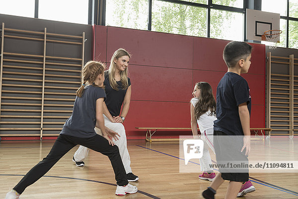 Teacher doing extension exercise with school children in sports hall  Munich  Bavaria  Germany