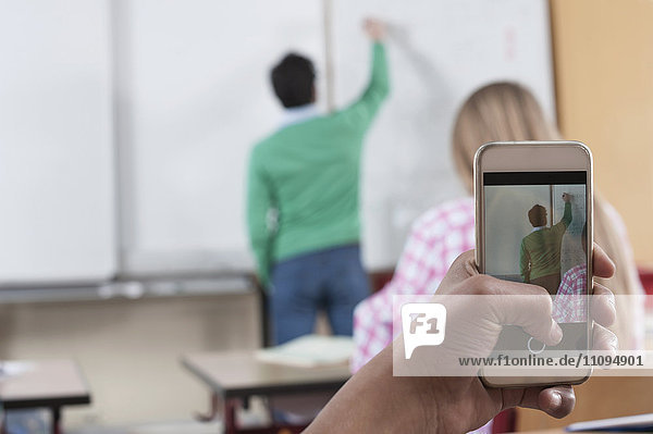 Lehrer unterrichtet im Klassenzimmer  während Schüler mit ihrem Smartphone ein Foto von ihm machen  Bayern  Deutschland