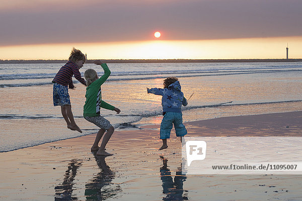 Three kids jumping on beach during sunset  Viana do Castelo  Norte Region  Portugal