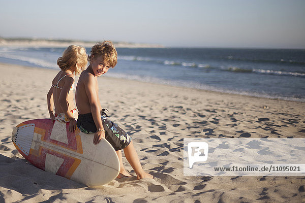 Two children sitting on bodyboard at the beach  Viana do Castelo  Norte Region  Portugal