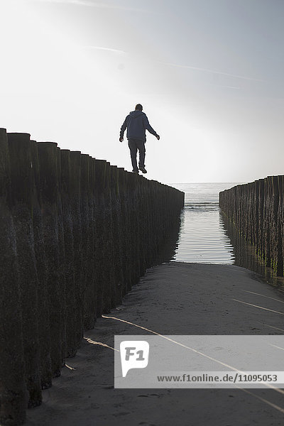 Silhouette eines reifen Mannes  der auf einem Holzpfosten am Strand balanciert  Renesse  Schouwen-Duiveland  Zeeland  Niederlande