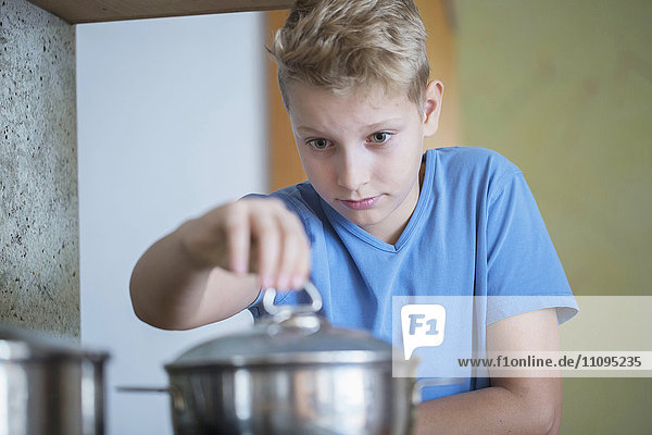 Boy opening lid of cooking pan carefully  Freiburg im Breisgau  Baden-Württemberg  Germany