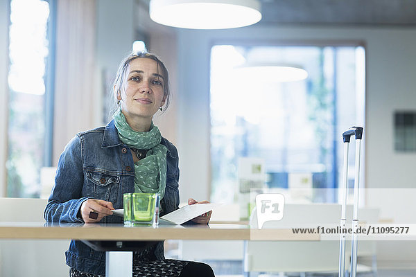 Mature female traveller with luggage sitting at table and looking at hotel menu Freiburg Im Breisgau Baden-Württemberg Germany