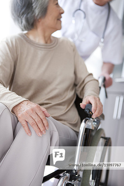 Ältere Frau im Rollstuhl sitzend blickt auf einen männlichen Arzt zurück