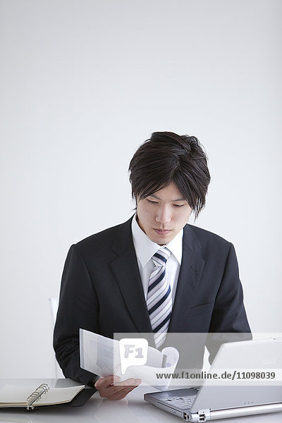 Young Man Reading Document and Using Laptop