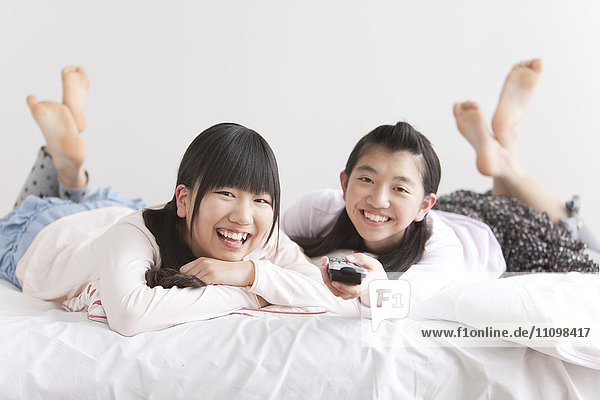 Zwei Teenager-Mädchen auf dem Bett liegend mit Fernbedienung
