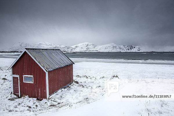 A typical house of the fishermen called rorbu on the snowy beach frames the icy sea at Ramberg  Lofoten Islands  Arctic  Norway  Scandinavia  Europe