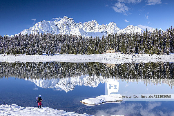 Hiker admires the snowy peaks and woods reflected in Lake Palu Malenco Valley Valtellina Lombardy Italy Europe