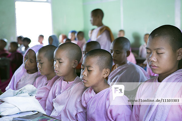 Buddhistische Schulanfängerinnen bei der Klassenmeditation im Klassenzimmer vor dem Unterricht  Sagaing  Myanmar  Südostasien