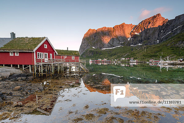 Fischerdorf und Berggipfel  die sich im Wasser unter der Mitternachtssonne spiegeln  Reine  Landkreis Nordland  Lofoten  Arktis  Nordnorwegen  Skandinavien  Europa