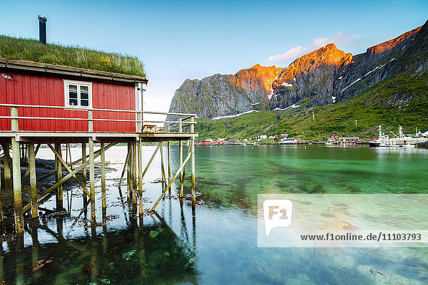 Typisches Fischerhaus namens Rorbu von der Mitternachtssonne beleuchtet  Reine  Landkreis Nordland  Lofoten  Arktis  Nordnorwegen  Skandinavien  Europa