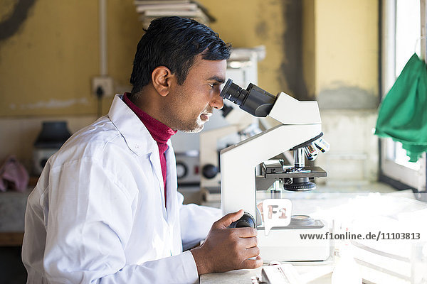 A lab technician working in a laboratory in a small hospital in Nepal looks into a microscope  Jiri  Solu Khumbu  Nepal  Asia