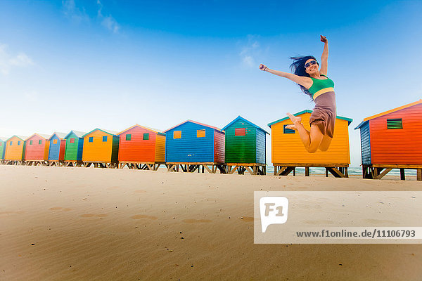 Laura Grier springt vor bunten Strandhütten  Muizenberg Beach  Kapstadt  Südafrika  Afrika