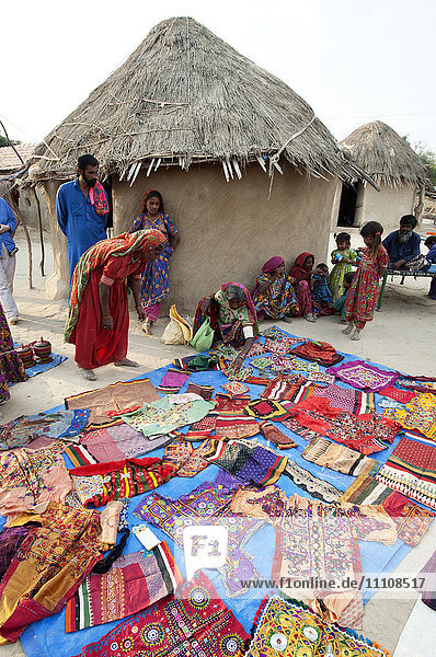 Pathan-Dorffrauen zeigen ihre traditionellen Stickereien vor Lehm- und strohgedeckten Stammeshäusern  Jarawali  Kutch  Gujarat  Indien  Asien