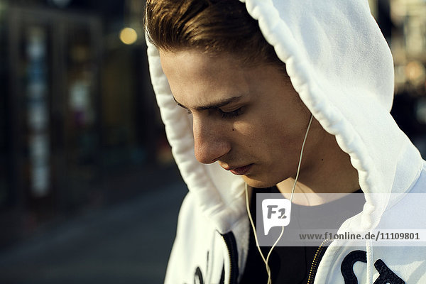 Close-up of teenage boy wearing hooded shirt listening music through headphones