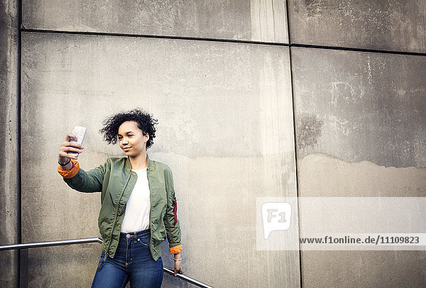Smiling teenage girl taking selfie while standing against weathered wall
