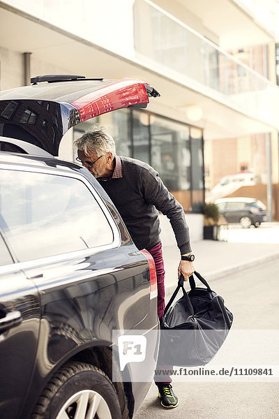 Senior Mann  der Gepäck aus dem Kofferraum nimmt  während er in der Stadt steht.
