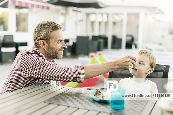 Smiling father feeding son while sitting at restaurant