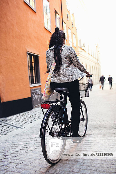 Rückansicht der Frau mit dem Fahrrad auf der Kopfsteinpflasterstraße