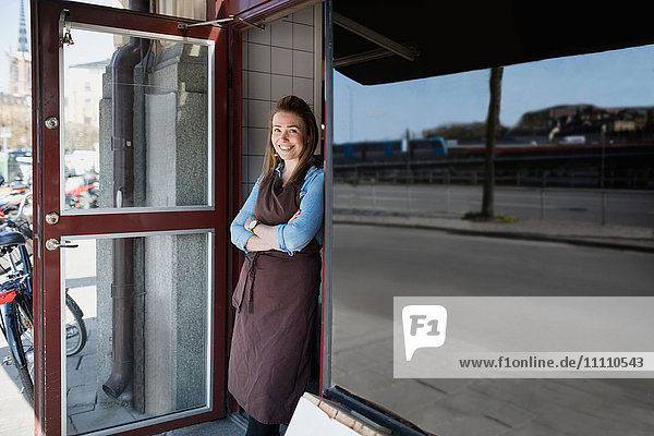 Portrait of confident owner wearing apron standing on store entrance