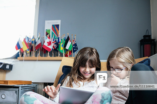 Lächelnde Freunde beim Sitzen auf dem Sofa in der Schule mit dem digitalen Tablett