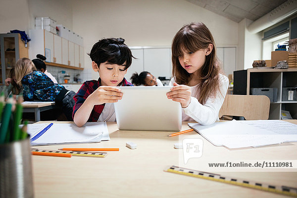 Konzentrierte Schüler mit digitalem Tablett am Schreibtisch im Klassenzimmer