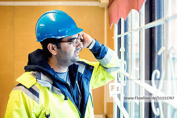 Construction worker talking on phone while standing by window in industry