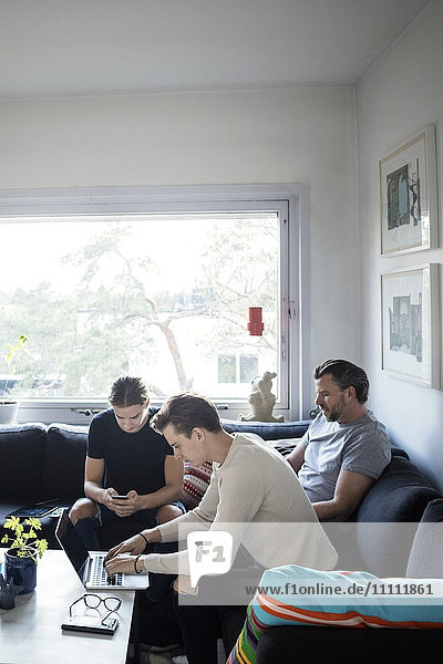 Männer  die Technologien nutzen  während sie mit ihrem Vater im Wohnzimmer sitzen.