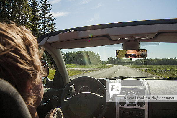 Schweden Uppland Mann fährt Auto auf der Landstraße bei Sonnenlicht