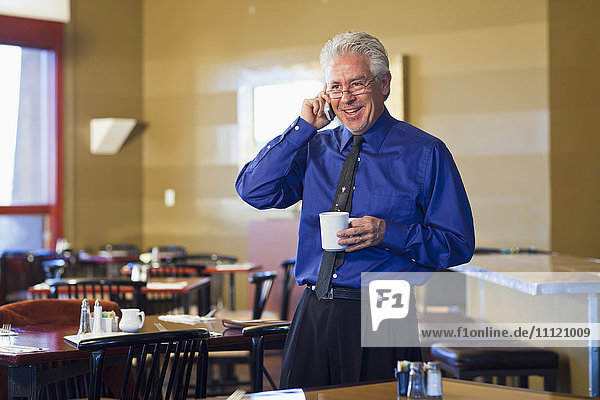Hispanischer Café-Besitzer  der mit seinem Handy telefoniert