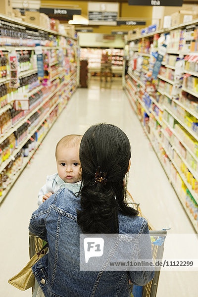 Asiatische Mutter kauft mit Baby im Lebensmittelgeschäft ein