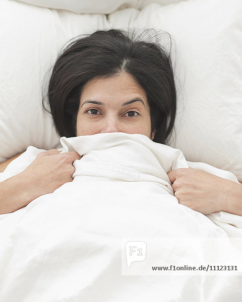 Hispanic woman in bed covering her face