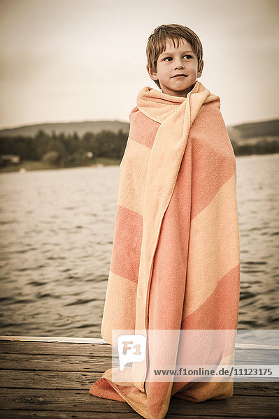 Caucasian boy wrapped in towel on wooden dock