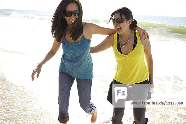 Grinning mixed race sisters hugging on beach