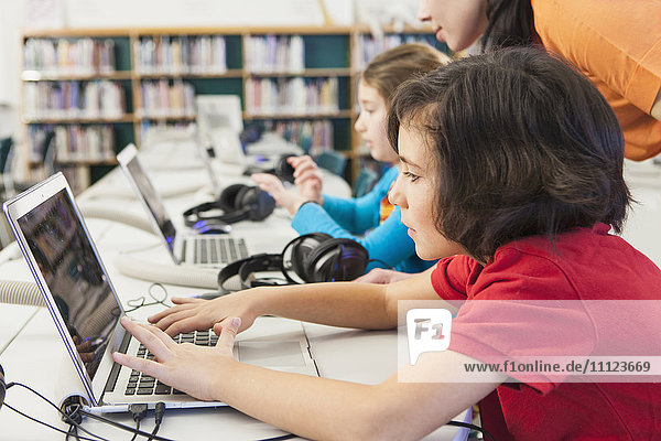 Kaukasische Kinder benutzen Laptops in der Bibliothek