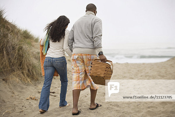 Paar  das am Strand mit Picknickkorb spazieren geht