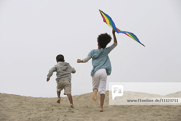 Mixed race children running on beach with kite