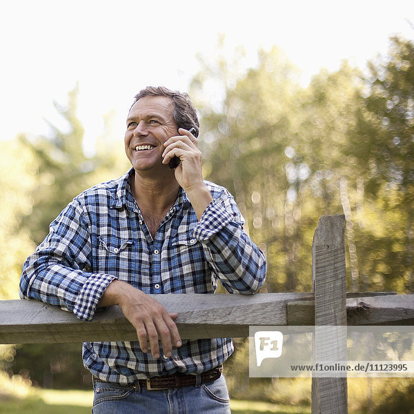 Caucasian man leaning on fence talking on cell phone