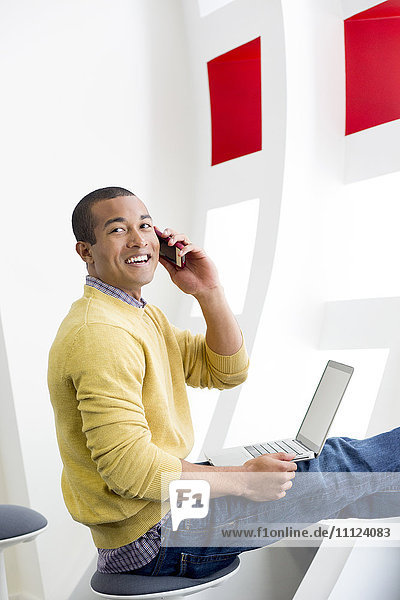 Mixed race man on laptop talking on cell phone