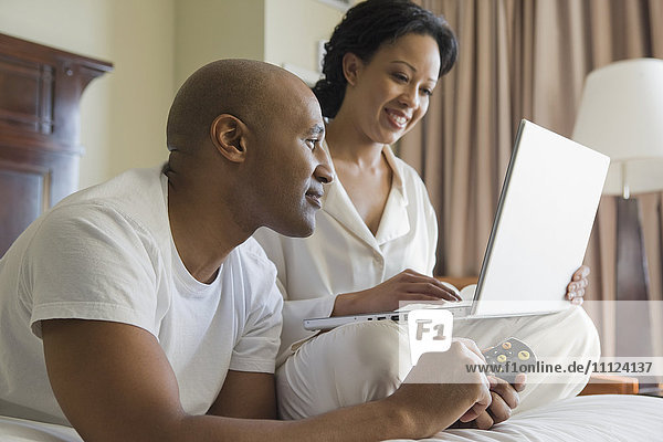 African couple in bed using laptop
