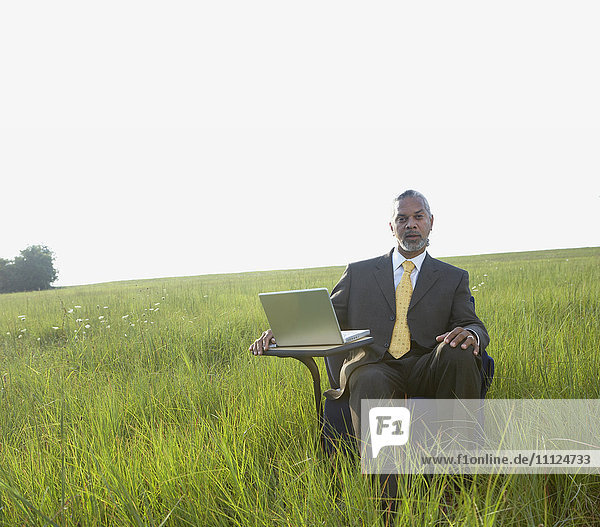 Afrikanischer Geschäftsmann sitzt mit Laptop auf einem Feld
