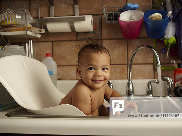 Mixed race baby girl bathing in sink