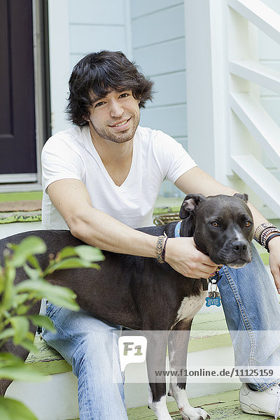 Mixed race man sitting on front stoop with dog