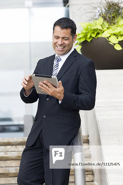 Hispanic businessman with tablet computer on city street
