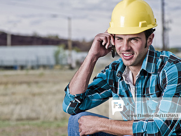 Lächelnder Bauarbeiter  der mit seinem Handy telefoniert