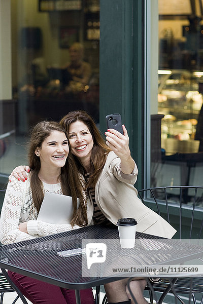 Caucasian mother and daughter taking picture in cafe