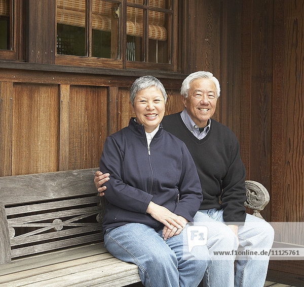 Älteres asiatisches Paar  das lächelnd auf einer Bank im Freien sitzt