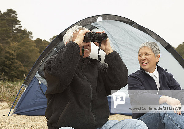 Älteres asiatisches Paar beim Zelten mit Ferngläsern
