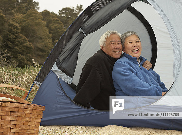 Älteres asiatisches Paar sitzt lächelnd im Zelt